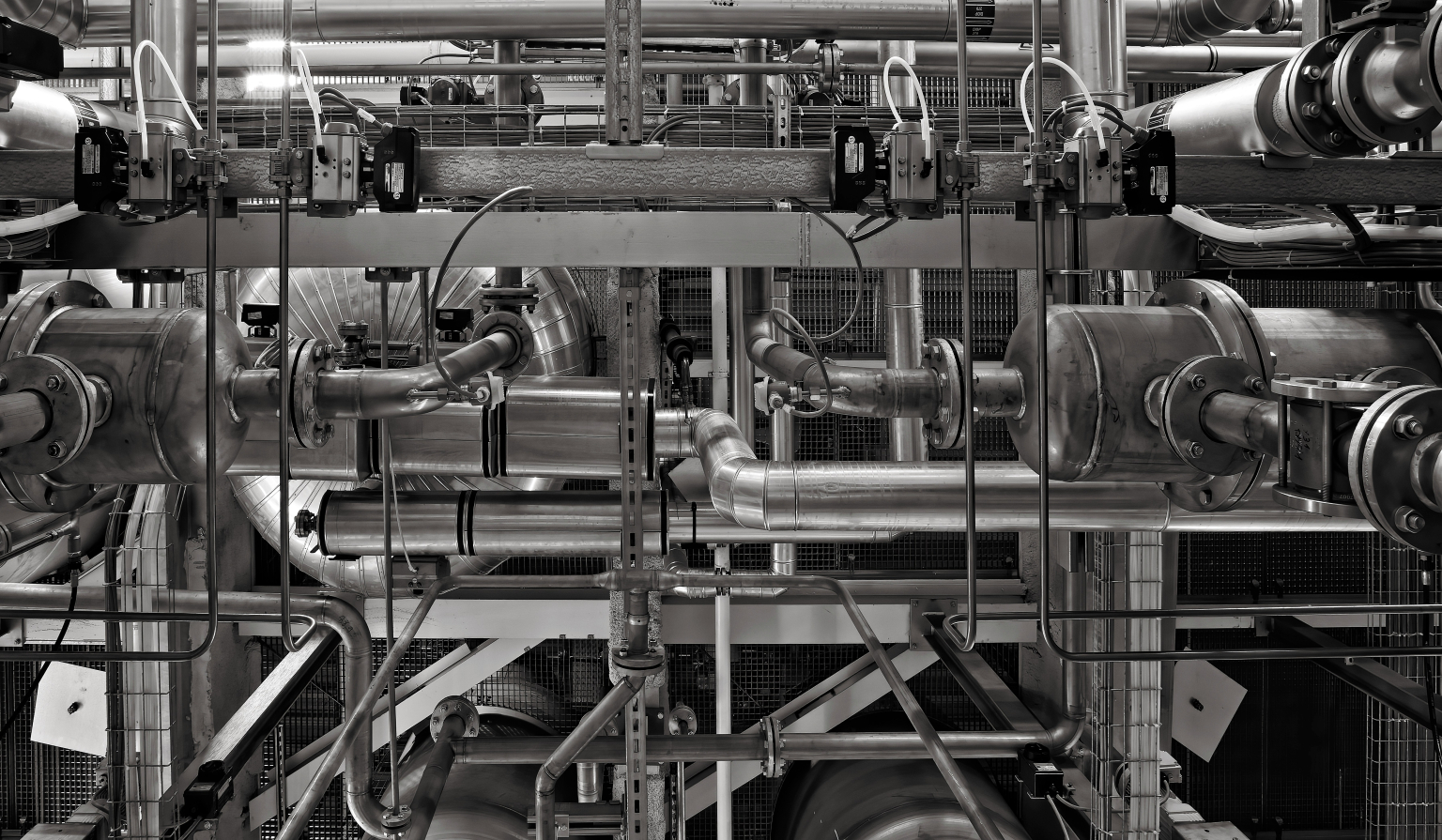 Et komplekst nettverk av industrielle rør, ventiler og metallstrukturer i et fabrikkmiljø